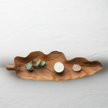 Top-down flat lay of handcrafted teakwood leaf tray Style 1 styled with eucalyptus, tea light candle and crystal on white linen — coastal home decor