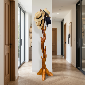 A sculptural wooden coat rack shaped like a tree trunk stands in a bright hallway, holding three straw hats and a dark navy hat.