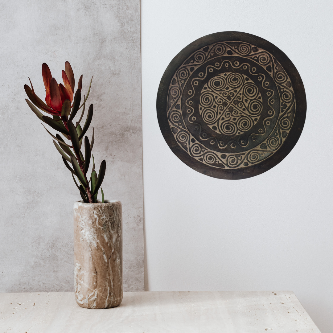 Decorative plate with intricate patterns on a white wall next to a vase with flowers.
