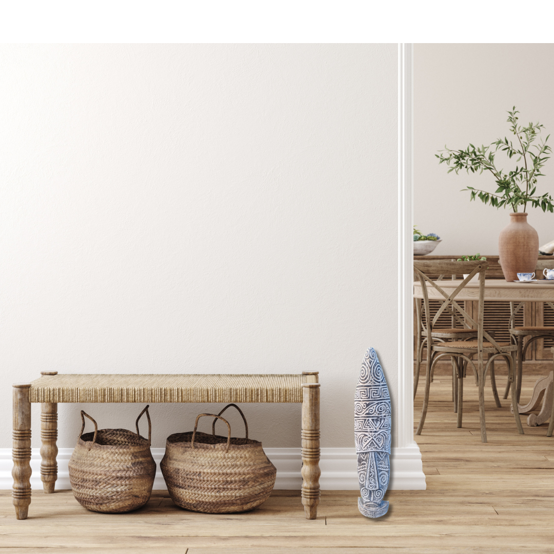Wooden bench with woven baskets and a decorative tribal mask statue   against a white wall.