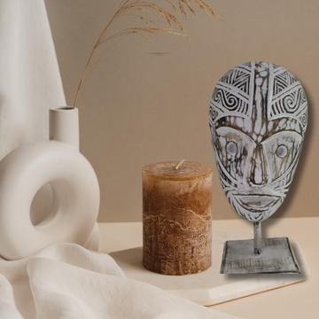 White-wash tribal wooden mask on stand styled with pillar candle and ceramic vase in earthy boho setting | Azure Decor
