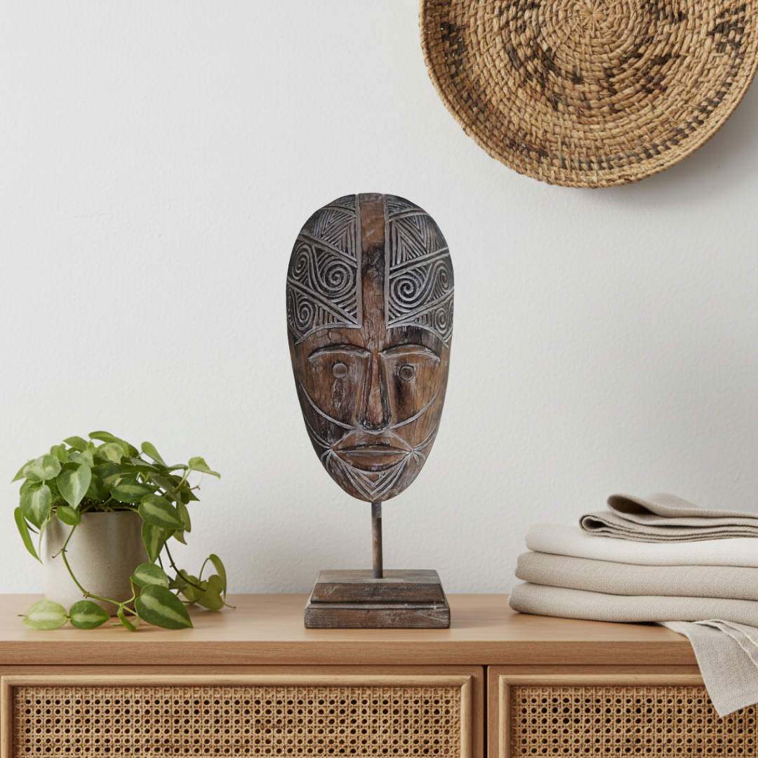 Dark carved decorative piece styled with trailing greenery, folded neutral linen and a woven wall basket