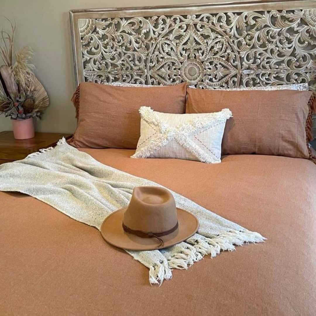 Bed with brown bedding, decorative headboard, and a hat on a blanket.