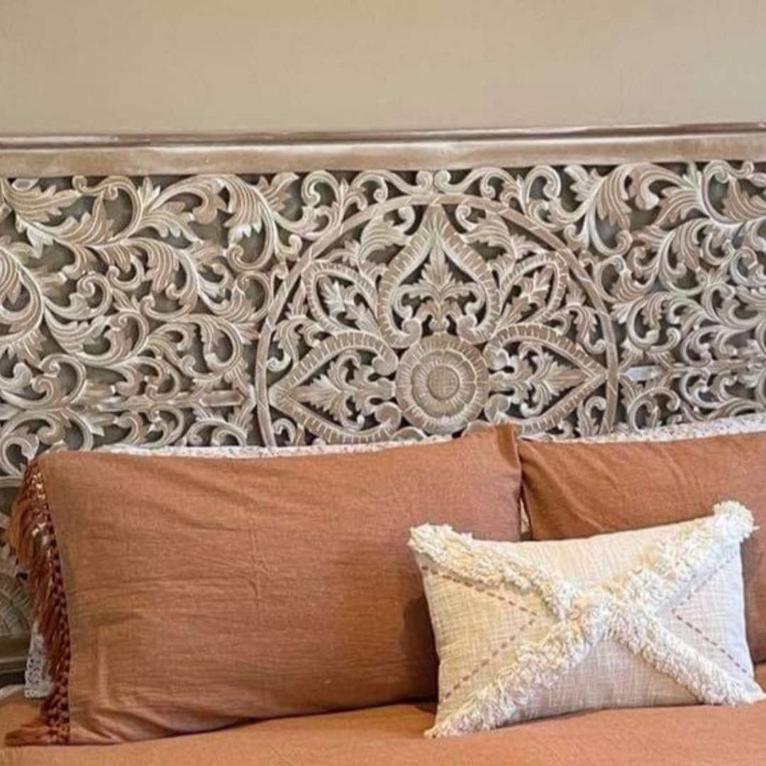 Decorative headboard with intricate carvings and pillows on a bed.