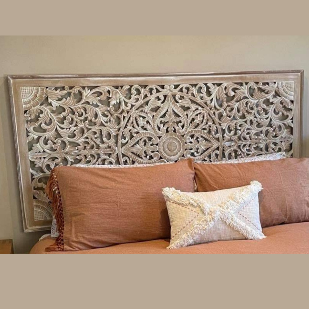 Decorative headboard with intricate carvings above a bed with pillows and a blanket.