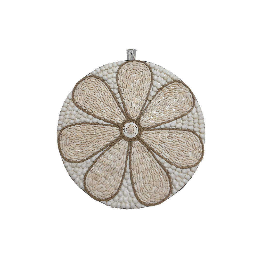 Round handcrafted wall art piece with a soft cream cowrie shell daisy petal pattern outlined in jute rope and a central spiral shell accent on a white shell base.