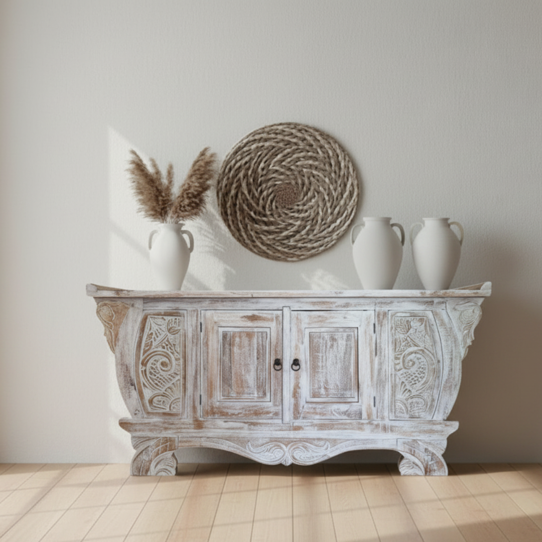 Whitewashed hand-carved Balinese teak entryway cabinet with ornate scrollwork, styled with pampas grass, white ceramic vases and seagrass wall art in coastal living room