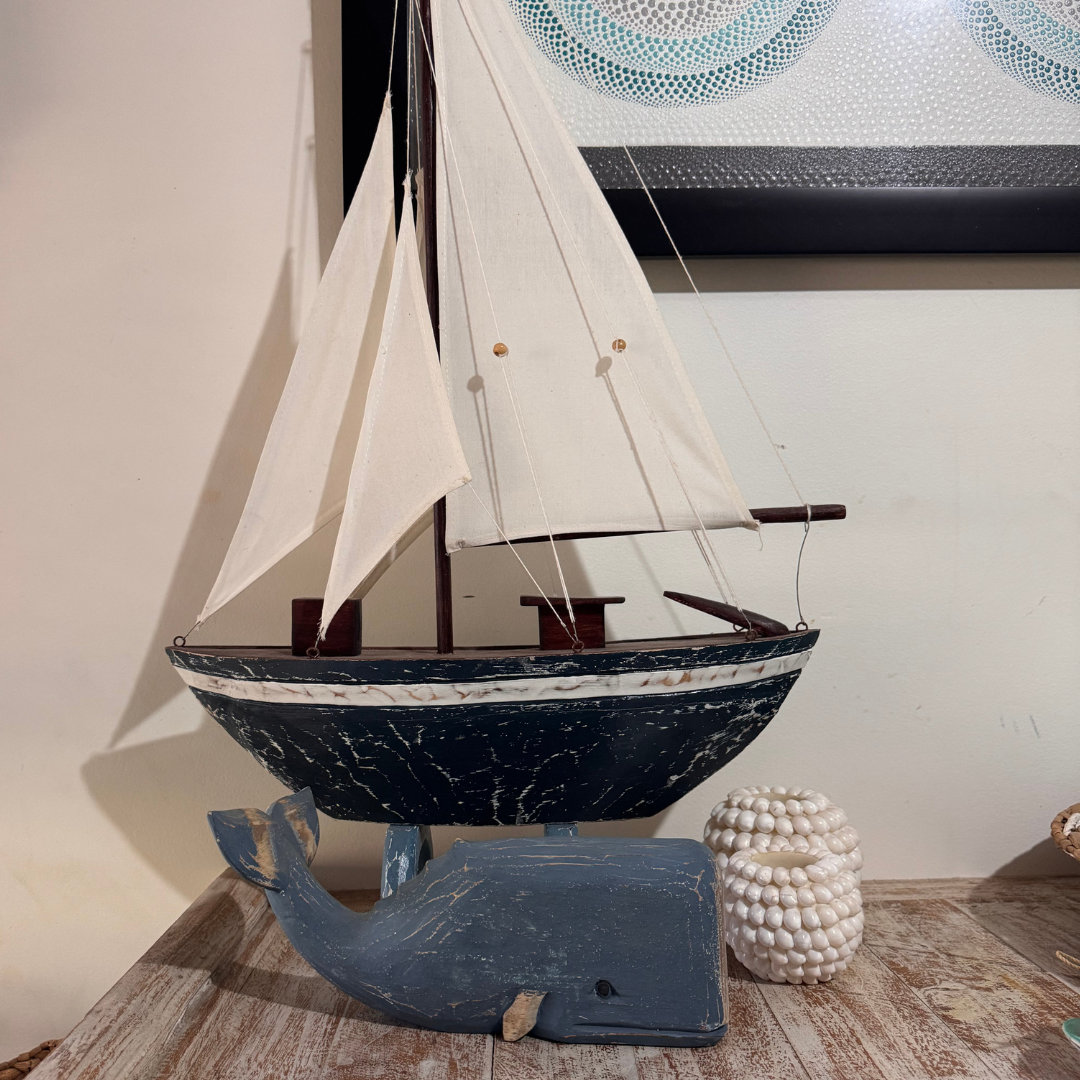 Model sailboat on a wooden base with a decorative whale, against a neutral wall.