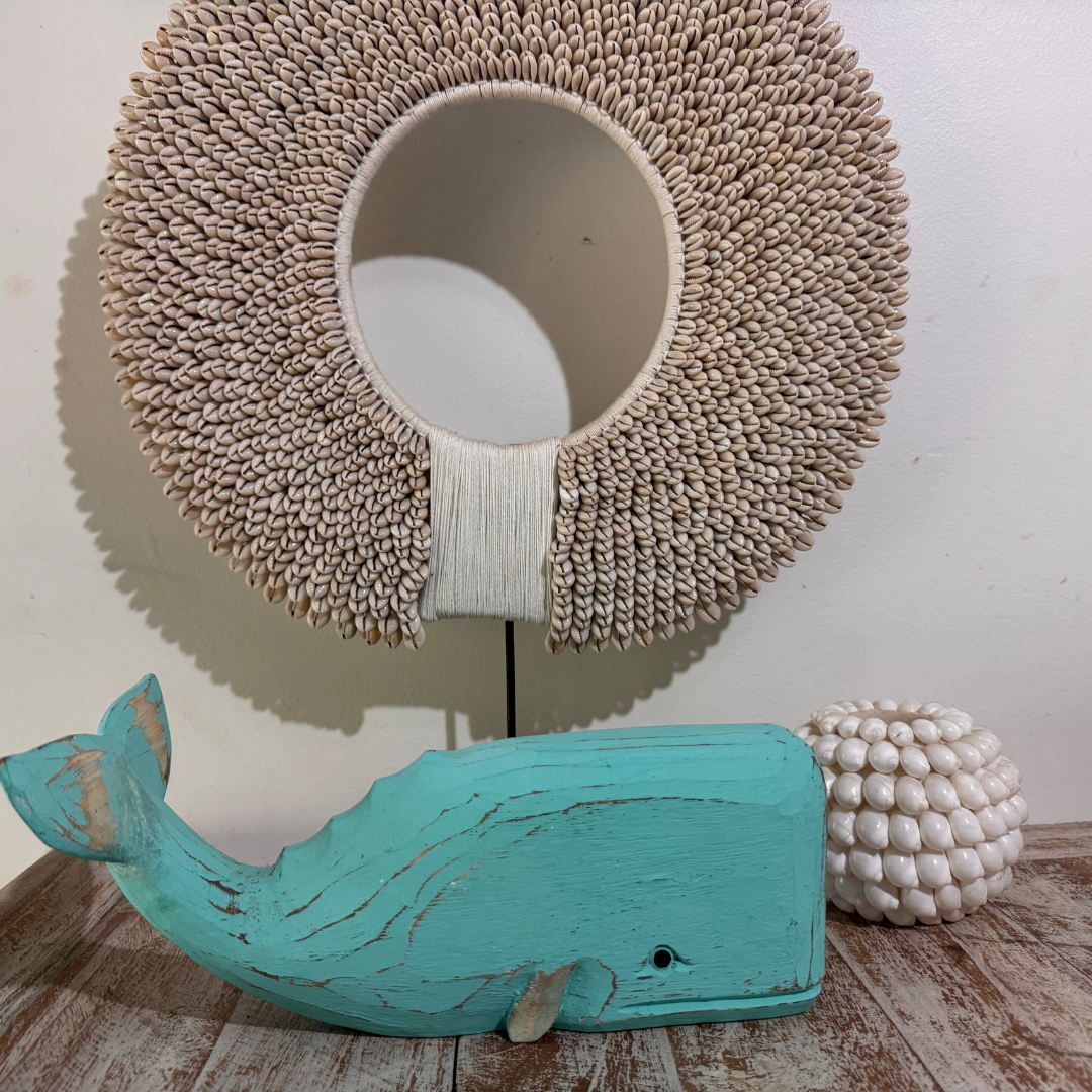 Decorative teal whale figure with a textured wall mirror and spherical decorative object on a wooden surface.