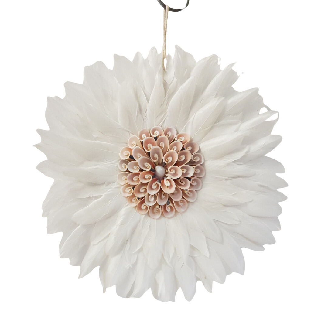 Close-up of a round white feather wall hanging with layered white feathers and a blush pink spiral shell centrepiece on a white background, hanging string visible at top