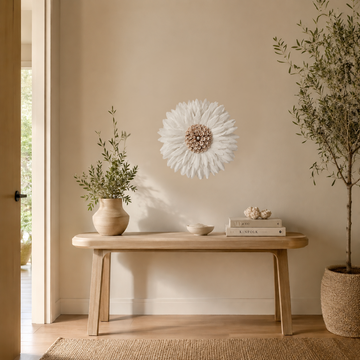 White JUJU hat wall art with a blush pink shell centre hung above a light timber console in a sunlit entryway, with an olive tree and a jute rug