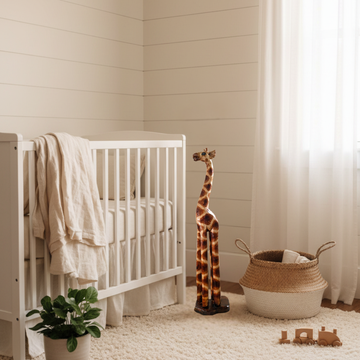 Tall carved timber figurine styled beside a white timber cot in a soft neutral baby nursery with warm natural light and woven decor accents