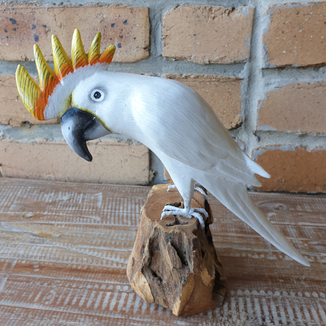 White cockatoo figurine on a wooden perch against a brick wall background