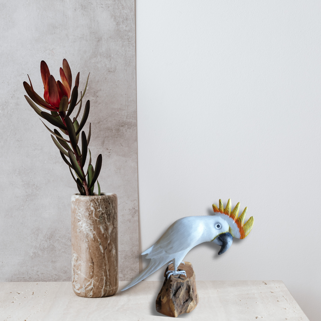 Decorative white cockatoo sculpture on a rock with a vase of flowers against a neutral background