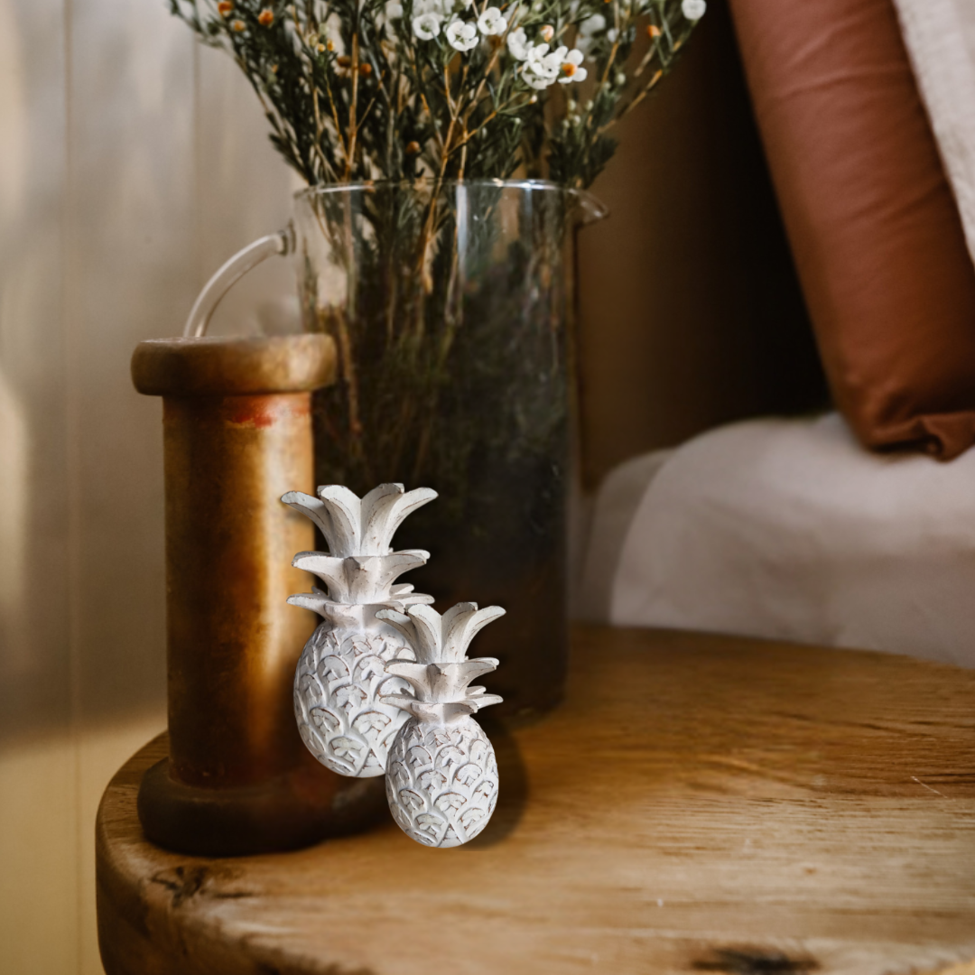 Decorative pineapple figurines on a wooden surface with a vase of dried flowers in the background.