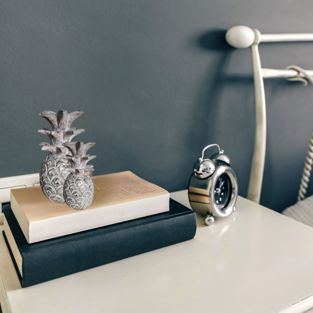 Decorative pineapple and clock on books with a plain background