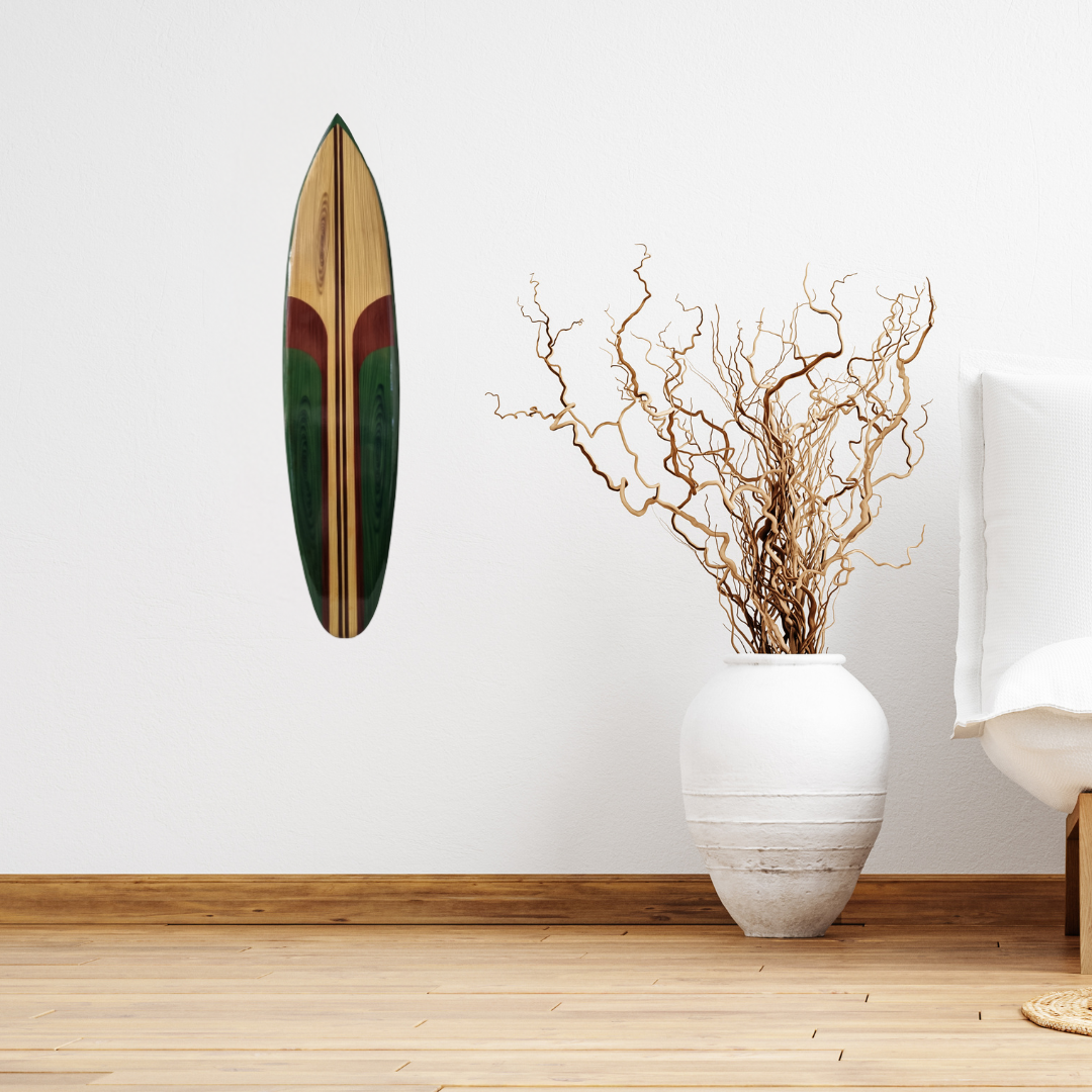 Wooden surfboard on a white wall with a vase containing branches on a wooden floor.