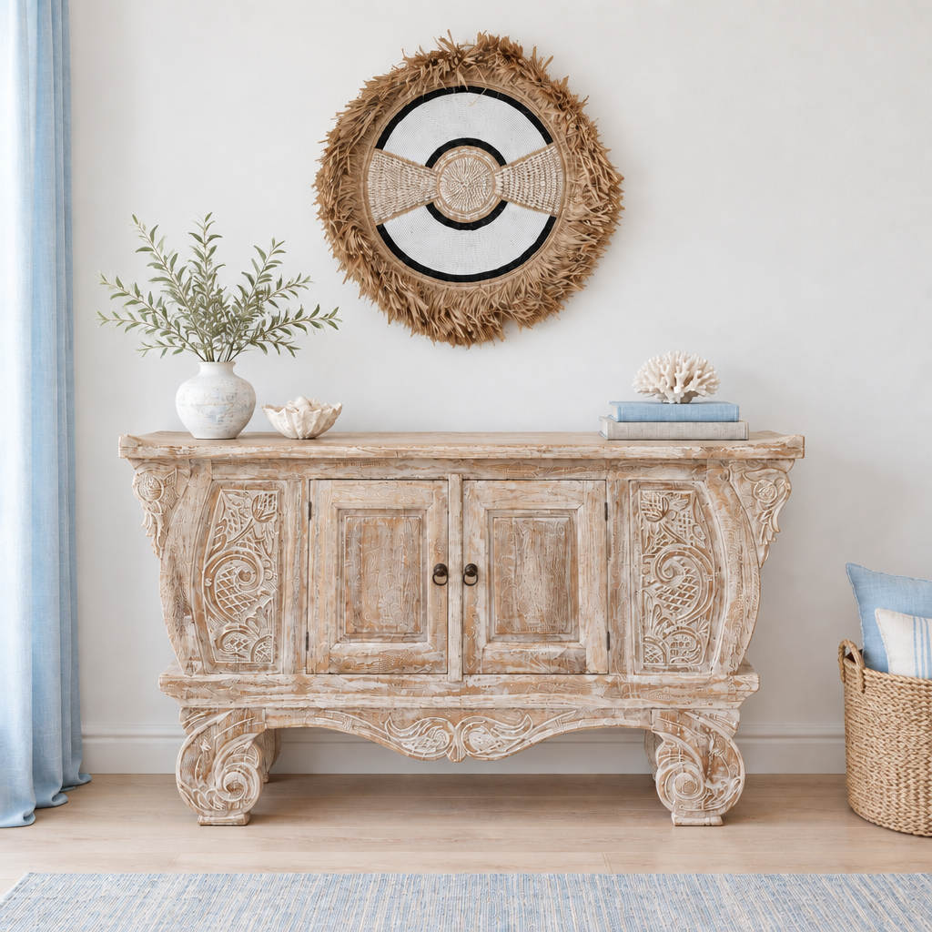 Black-ringed shell and bead wall hanging above a weathered carved cabinet in a light coastal room