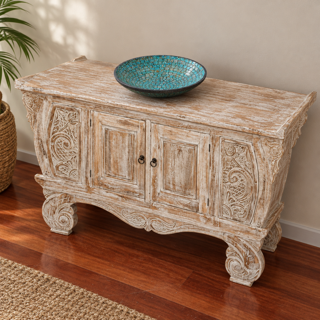 Whitewashed carved timber cabinet styled in a sunlit hallway with a leafy plant, timber flooring and a woven rug.