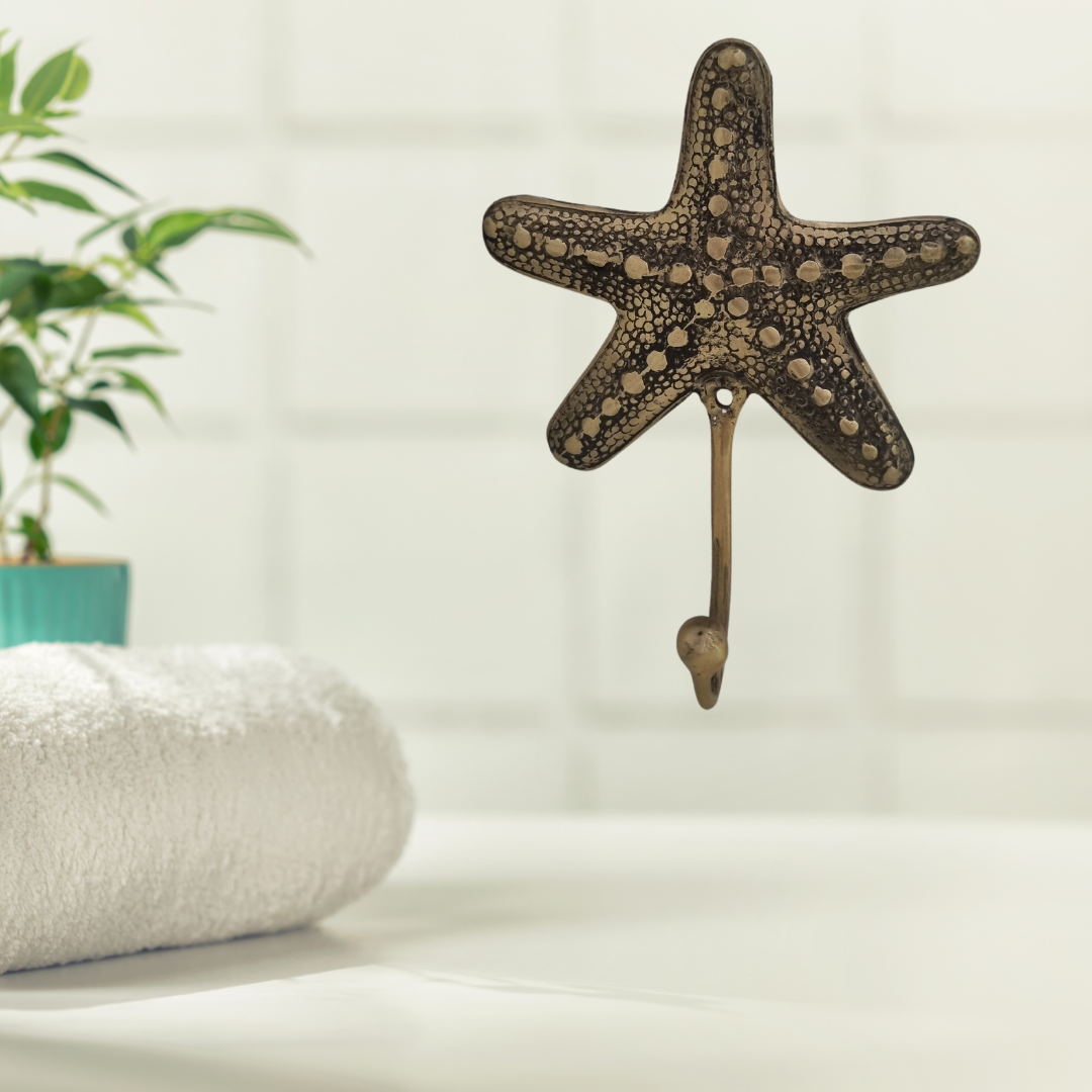 Brass starfish wall hook mounted above a folded white towel in a bright coastal bathroom