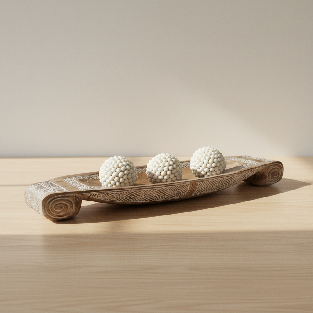 Three white shell balls arranged in a row inside a long hand-carved timber dish on an oak console