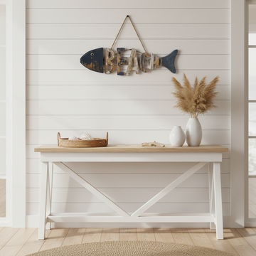 carving hung on white shiplap wall above a coastal console table styled with white ceramic vases, dried pampas grass and a woven rattan tray