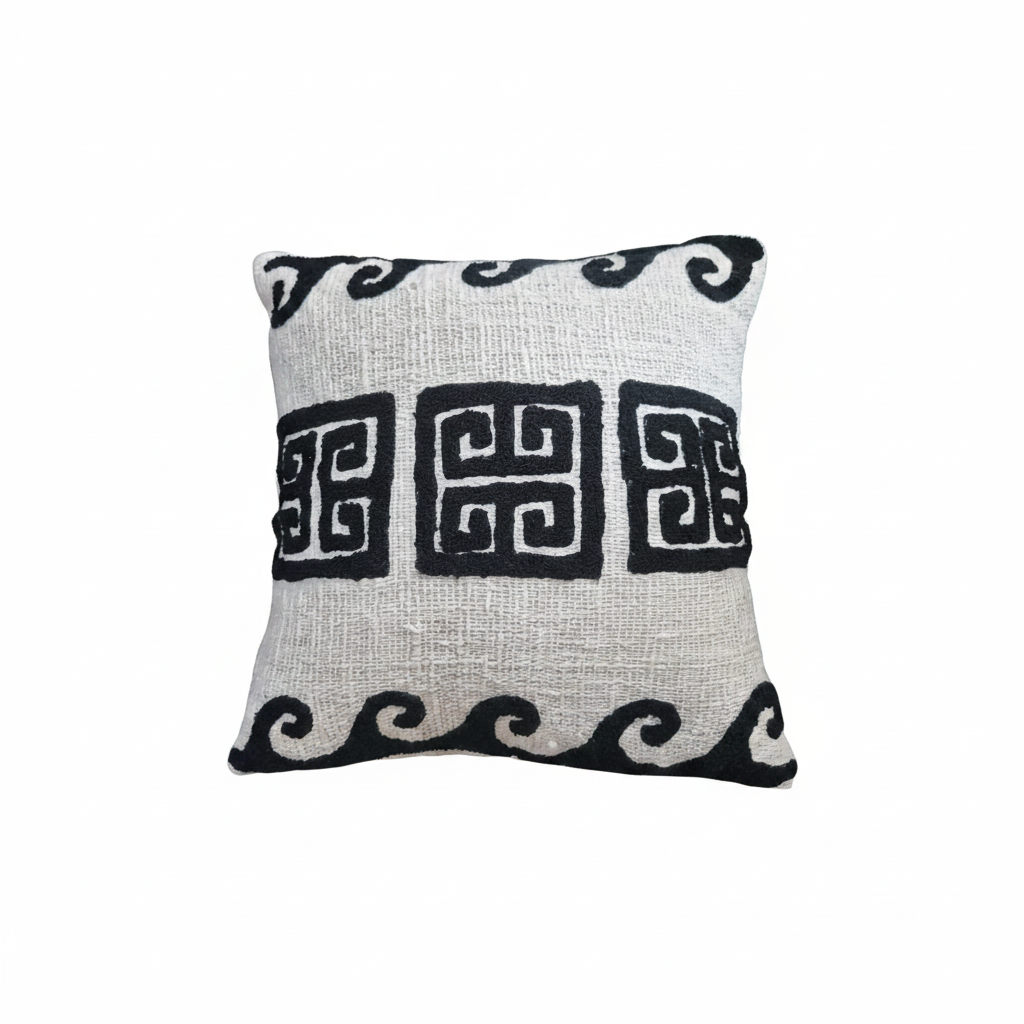 A square throw pillow with a textured off-white linen-like fabric, featuring a black geometric Greek key pattern across the center and black scrollwork borders at the top and bottom.