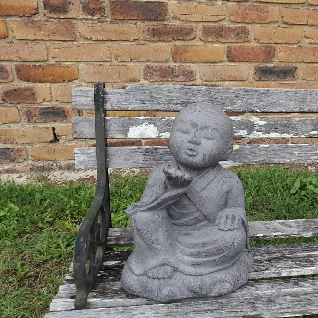 grey seated figure with closed eyes and an upturned palm on a wooden garden bench beside grass
