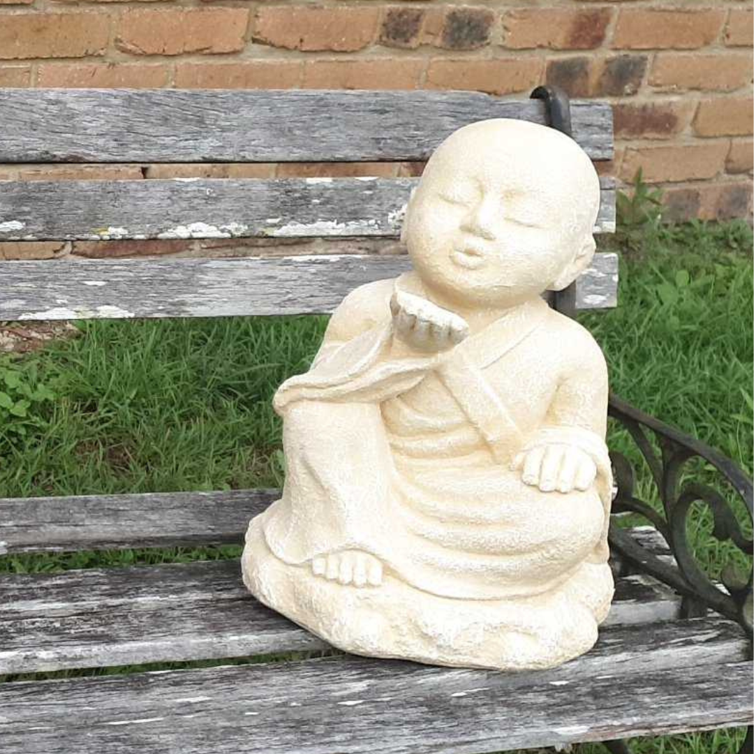 Cream seated figure with closed eyes and an upturned palm on a wooden garden bench beside grass