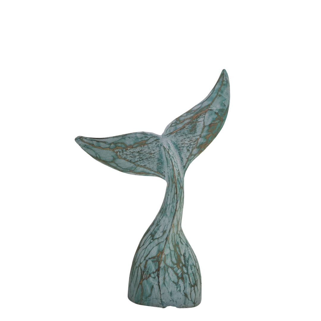 A handcrafted wooden carving of a whale tail with turquoise tones with a rustic wash finish on a white wall 