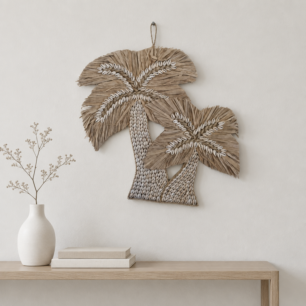A woven palm tree wall hanging in natural straw tones hangs on a light neutral wall above a wooden console table with a white vase and books.