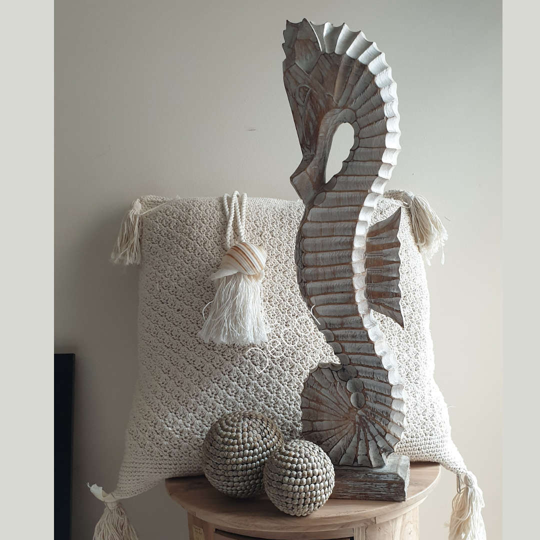 Decorative wooden sculpture on a round wooden table with a textured white pillow and spherical objects.