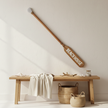 Long timber wall sign mounted diagonally above a console with woven baskets in a bright coastal entryway
