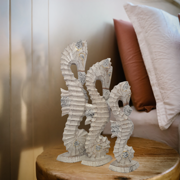 Decorative seahorse sculptures on a wooden surface with pillows in the background