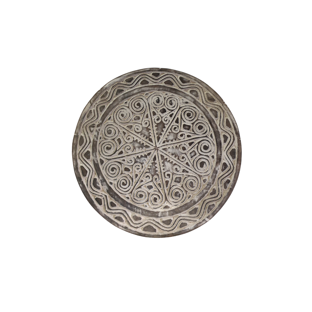 A photo shot of a rustic wooden circular wall hanging with whitewash finish on a white wall, tribal-inspired décor