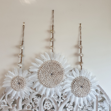 Three jute hanging strands with natural shell beads, styled above white feather and cowrie shell discs on a carved timber panel.