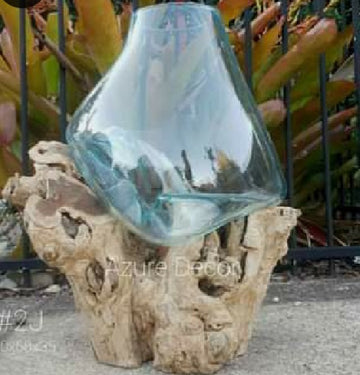 A large slumped glass vase on a natural driftwood base, with a blue tint to the glass.
